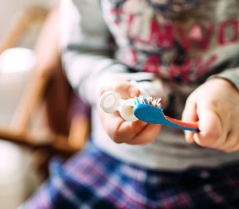 child applying toothpaste to toothbush