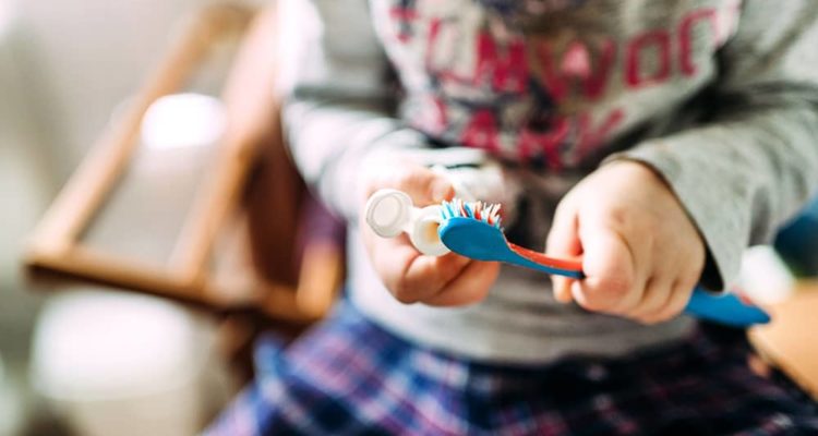 child applying toothpaste to toothbush