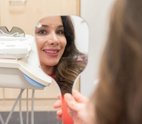 Woman checking her teeth in the mirror after procedure.