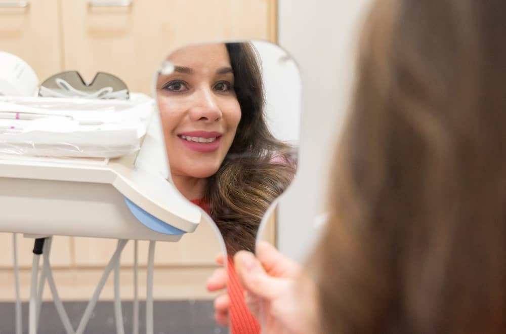 Woman checking her teeth in the mirror after procedure.