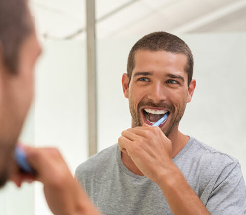 man with veneers brushing teeth in mirror