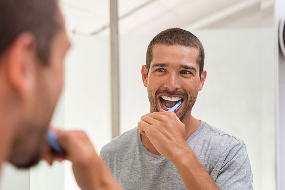 man with veneers brushing teeth in mirror