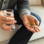 man holding a range of different vitamins and a glass of water
