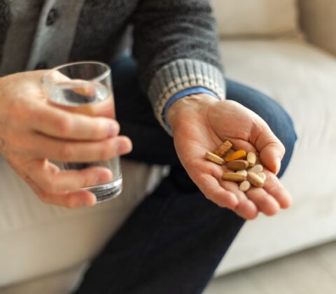 man holding a range of different vitamins and a glass of water