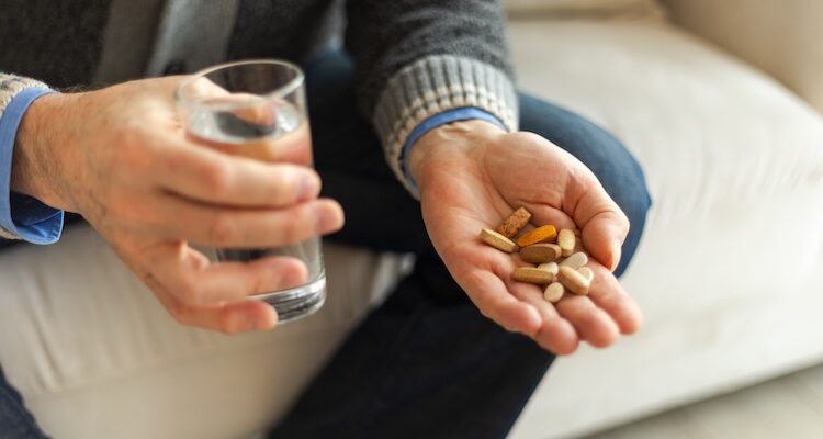 man holding a range of different vitamins and a glass of water